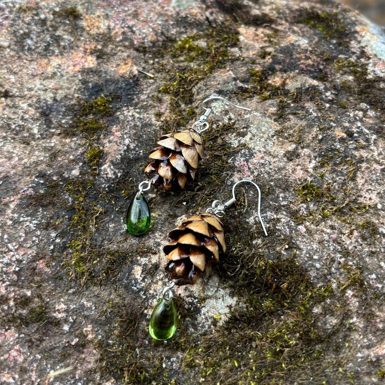 a pair of earrings made from hemlock pinecones with green glass teardrop beads on earring hooks