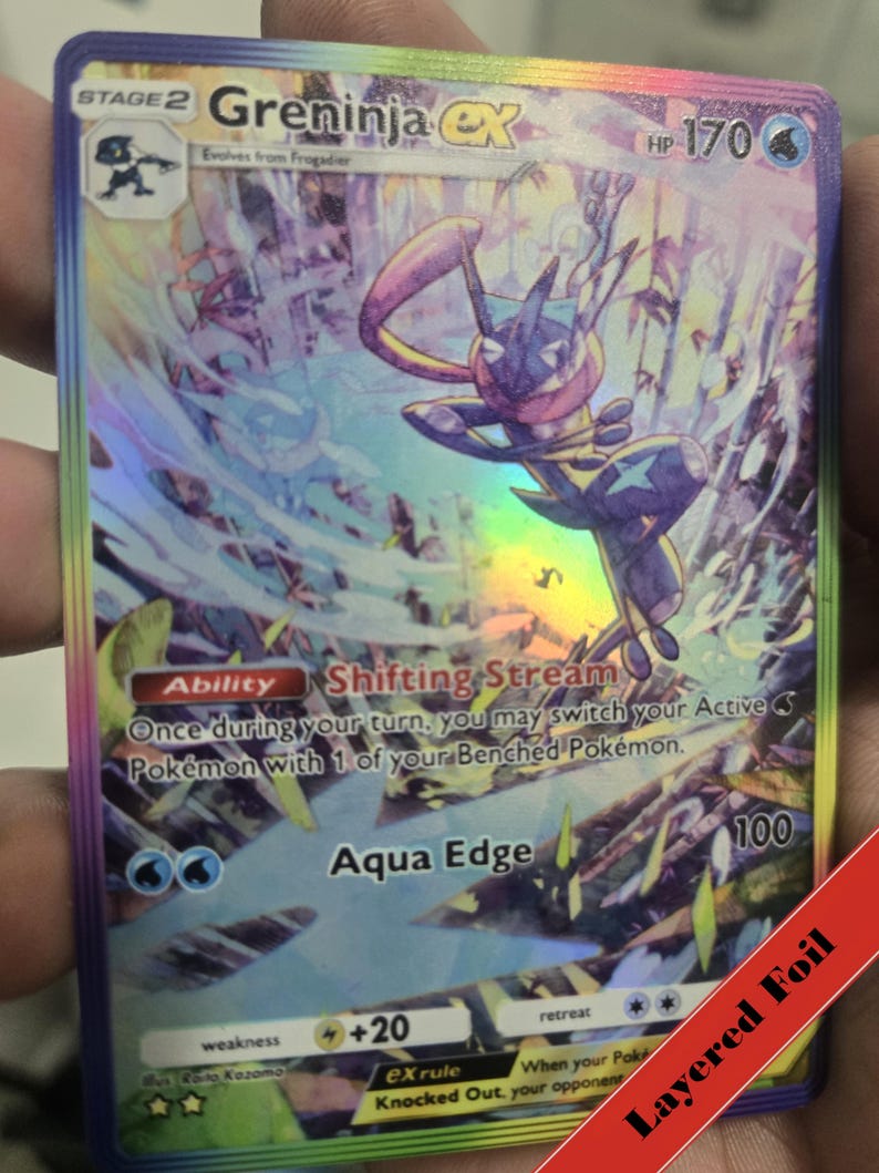 Puede incluir: Una carta coleccionable hologr&aacute;fica de Greninja EX, evoluci&oacute;n de fase 2 de Frogadier con 170 HP. La carta muestra la habilidad Shifting Stream y el ataque Aqua Edge, con un borde de l&aacute;mina arco&iacute;ris y una ilustraci&oacute;n din&aacute;mica del personaje.