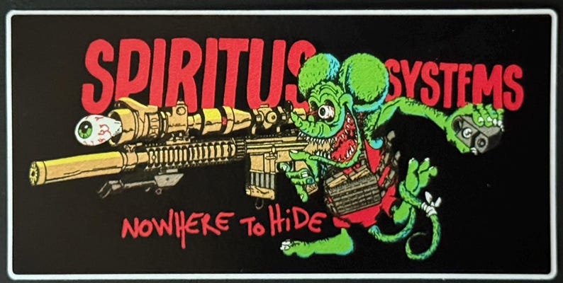Op de afbeelding: Zwarte rechthoekige sticker met een cartoonrat die een geweer vasthoudt en de rode tekst "SPIRITUS SYSTEMS". De groene rat heeft een rood vest en een wijd open mond. De tekst "NOWHERE to HIDE" is ook in het rood.