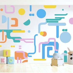 Könnte beinhalten: Eine weiße Wand mit einem bunten geometrischen Muster aus blauen, gelben, rosa, orangen und grünen Formen. Die Wand ist mit einem blauen, gelben und rosa abstrakten Design verziert. Vor der Wand stehen auch zwei Spielzeugblöcke, auf denen "K" und "D" steht.
