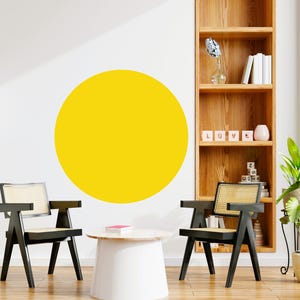 May include: A yellow circle wall decal on a white wall with two black chairs and a white round table in front of a wooden bookshelf with the word "LOVE" spelled out in blocks.