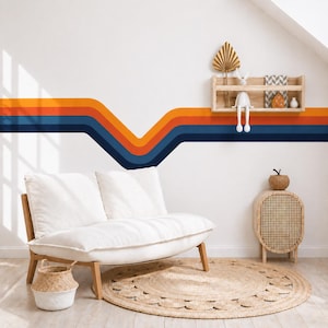 May include: A white room with a retro-style wall design featuring horizontal stripes in navy blue, orange, and a lighter orange. A white loveseat with wooden legs sits on a round jute rug. A small wooden shelf holds decorative items, and a woven cabinet is nearby.