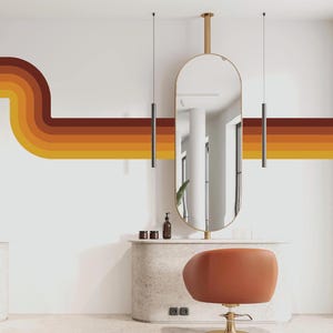 May include: A white wall with a curved, multi-colored stripe design in shades of orange, yellow, and brown. A large oval mirror hangs on the wall above a white vanity table with a brown leather chair.