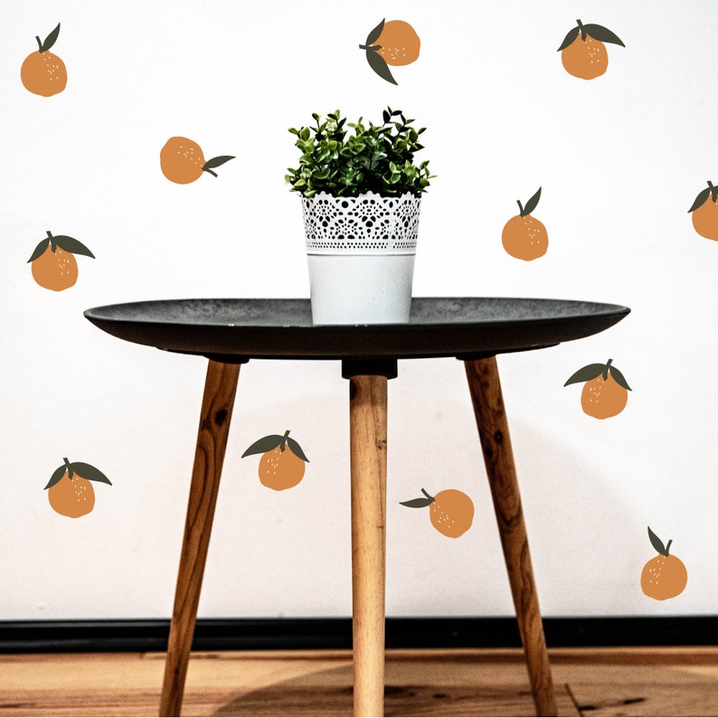 May include: A small potted plant sits on a black side table with a white background. The background is decorated with orange fruit stickers.