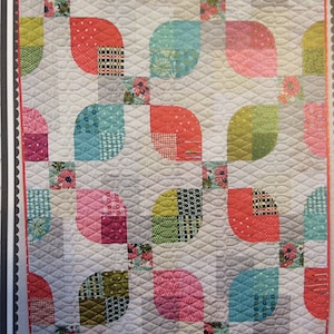 May include: A quilt with a patchwork design featuring a variety of colorful fabrics. The quilt is made up of curved shapes that resemble leaves. The quilt is a light gray color with a subtle texture.