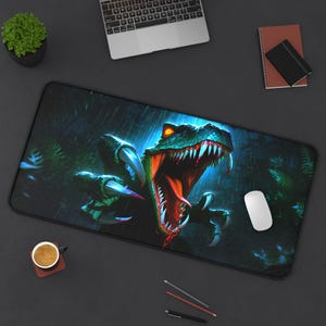 May include: A rectangular black mousepad featuring a detailed illustration of a green dinosaur with an open mouth, sharp teeth, and glowing orange eyes. The background depicts a dark, rainy forest scene.