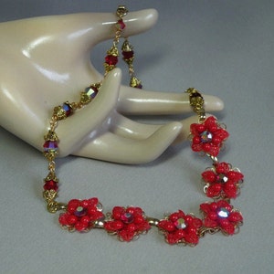 May include: A red and gold beaded necklace with flower-shaped accents. The necklace is made with small red beads and gold chain links. The flower accents are made with red beads and gold wire.