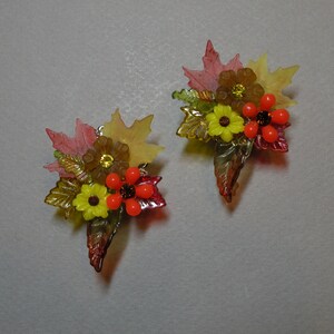 May include: A pair of earrings featuring a cluster of autumn-themed flowers and leaves in shades of red, orange, yellow, and green.