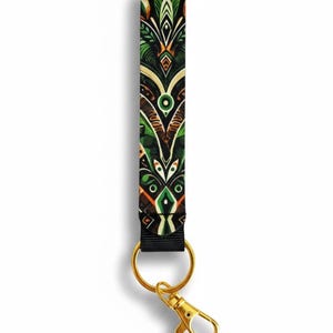 May include: A black lanyard with a gold-colored clasp and key ring. The lanyard features a repeating pattern of green, brown, and orange geometric shapes. The design is symmetrical and detailed.