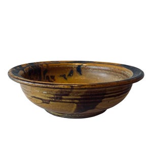 May include: A brown ceramic bowl with a dark brown rim and glaze. The bowl has a rustic, handmade look.