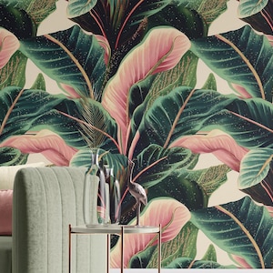 Puede incluir: Un vibrante papel pintado con un patrón repetido de grandes hojas tropicales en tonos verdes, rosas y dorados. Las hojas tienen venas prominentes sobre un fondo crema. Un sofá verde con cojines y una pequeña mesa con jarrones en primer plano.