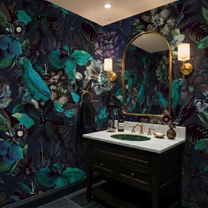 May include: A bathroom with dark floral wallpaper featuring teal parrots and large flowers. A dark wood vanity with a marble countertop and a green sink is below a gold-framed mirror. Gold sconces and fixtures complete the look.