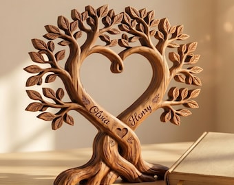 Op de afbeelding: Bruine houten boomsculptuur met een hartvormige opening, met de namen "Olivia" en "Henry" gegraveerd. De sculptuur staat op een houten oppervlak, naast een gesloten boek.