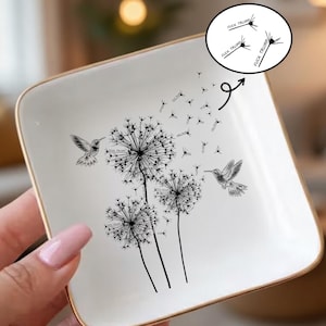 May include: Square white ceramic trinket dish with a gold rim. The dish features a black and white dandelion design with hummingbirds. The text "FUCK TRUMP" is in a speech bubble.