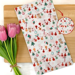 May include: White Christmas-themed kitchen towel with a repeating pattern of string lights, reindeer, Christmas trees, and candy canes. The lights spell out "FUCK TRUMP". A bundle of pink tulips rests on a wooden cutting board.