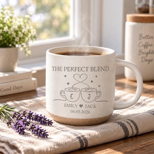 May include: A cream-colored ceramic mug with a speckled finish and a natural clay base. The front features the text THE PERFECT BLEND, two line-art coffee cups with the letters E and J, the names EMILY and JACK with a heart, and the date 06.05.2026.