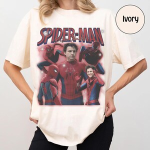 K&ouml;nnte beinhalten: Elfenbeinfarbenes T-Shirt mit einem Spider-Man-Motiv und dem Text "Spider-Man Peter Parker". Das Design umfasst mehrere Bilder von Spider-Man in seinem rot-blauen Anzug. Das Shirt hat kurze &Auml;rmel und einen Rundhalsausschnitt.
