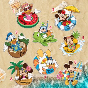 May include: A collection of colorful cartoon character stickers featuring Mickey Mouse, Donald Duck, and Goofy in various beach and summer-themed designs. Characters are shown with floaties, surfboards, and tropical accessories. Names are written on some of the stickers.
