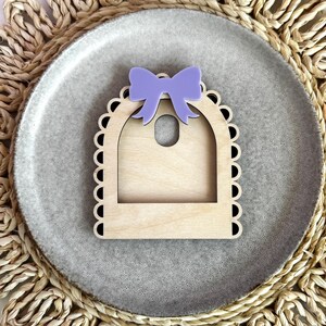May include: A wooden picture frame with a scalloped edge and a purple bow on top. The frame is designed to hold a small photo or other decorative item.