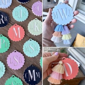 Pu&ograve; includere: Una collezione di portachiavi personalizzati in vari colori pastello, ognuno con un'iniziale o monogramma unico. I portachiavi hanno un bordo smerlato e sono adornati con accenti di nappe colorate. I portachiavi sono in acrilico.