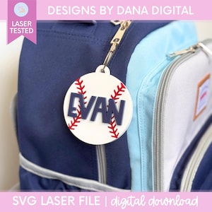 May include: A circular white acrylic baseball-themed bag tag featuring red stitched detailing and the name EVAN in raised dark blue capital letters. The tag is attached to the zipper of a navy blue and light blue backpack with a metal clip.
