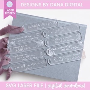May include: A collection of eight clear acrylic rectangular bookmarks featuring white engraved inspirational quotes and floral or celestial illustrations. Each bookmark has a hole at one end, with several tied with dusty rose silk ribbons.