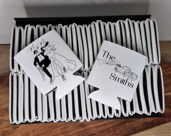 Puede incluir: Enfriadores de latas blancos con ilustraciones de líneas negras. Uno presenta una pareja bailando con el texto "M & M". El otro tiene un coche antiguo con el texto "The Smiths". Los enfriadores están apilados sobre una base a rayas blancas y negras.