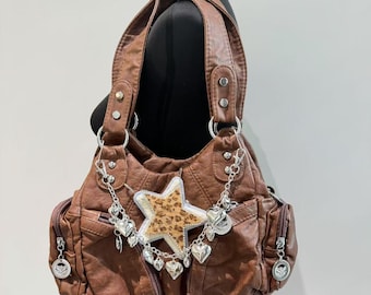 May include: A brown faux leather handbag with a star-shaped patch and silver heart charms hanging from the zipper pulls.