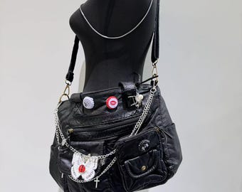 May include: A black leather shoulder bag with multiple pockets and zipper closures. The bag is decorated with silver chains, a butterfly charm, and bottle cap accents.