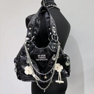 May include: Black faux leather handbag with silver chain straps and charms. The bag has a patch that reads "My Mom Thinks I'm Special".