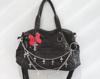 May include: A black leather satchel handbag with a silver chain strap adorned with silver cross charms. The bag has a red and black embroidered embellishment on the front.