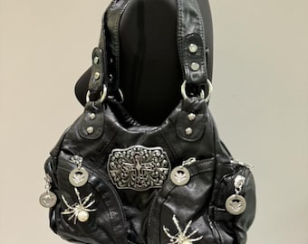 May include: Black leather handbag with silver spider and cross embellishments. The bag has a zip closure and a top handle.