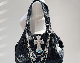 May include: Black leather handbag with a silver cross adorned with colorful jewels. The bag has multiple zippered compartments and silver chain accents.
