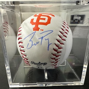May include: A white baseball with red stitching and an orange logo, displayed in a clear acrylic case. The baseball features a blue signature and the Rawlings logo. The orange logo is the San Francisco Giants logo.