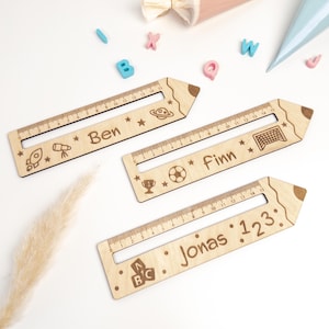 Drei personalisierte Lesehilfen aus Holz mit Lineal liegen auf hellem Hintergrund. Die Leselineale sind mit den Namen „Ben“, „Finn“ und „Jonas“ sowie Weltraum-, Fußball- und ABC-Motiven graviert – ideal als Geschenk zur Einschulung oder als Inhalt für die Schultüte.