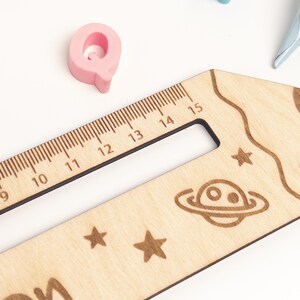 Nahaufnahme einer personalisierten Lesehilfe aus Holz mit Lineal und Weltraum-Motiv. Zu sehen sind die gravierte Zentimeterskala, Sterne und ein Planet – ein praktisches Leselineal für Kinder zur Einschulung.