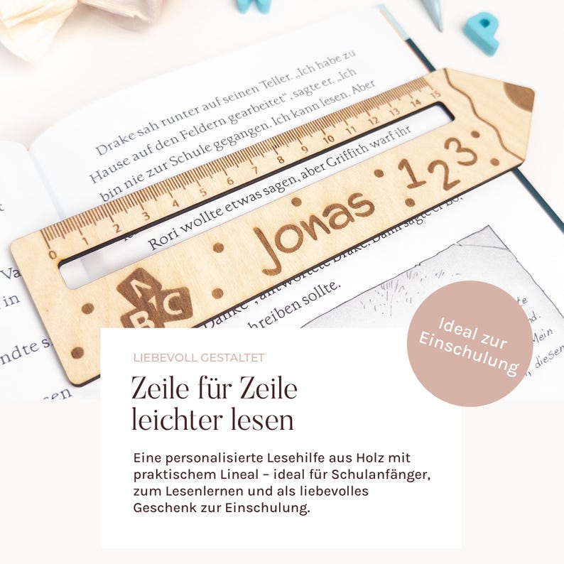 May include: A wooden bookmark shaped like a pencil, featuring a ruler, the name "Jonas", and the numbers "123". The bookmark is placed on an open book. The bookmark is light brown in colour.
