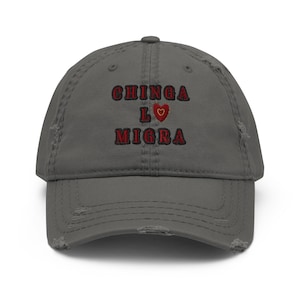 May include: Distressed gray baseball cap with the embroidered text "CHINGA LO MIGRA" in red, with a red heart symbol. The cap has a pre-worn look with distressed edges.