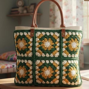 May include: A handmade tote bag with a crochet design. The bag features a green, yellow, and white floral pattern. It has a cream-colored interior and brown leather handles. The bag is sitting on a wooden surface.
