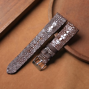 May include: Two brown watch straps with a textured, dotted pattern and white accents. One strap has a silver buckle. The straps are made of a material that resembles stingray skin.