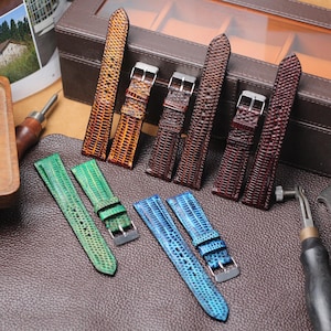 Puede incluir: Una colección de correas de reloj en varios colores, incluyendo naranja, marrón, verde y azul. Las correas tienen un patrón texturizado similar al de un reptil y hebillas de acero inoxidable. Están dispuestas sobre una superficie de cuero marrón.