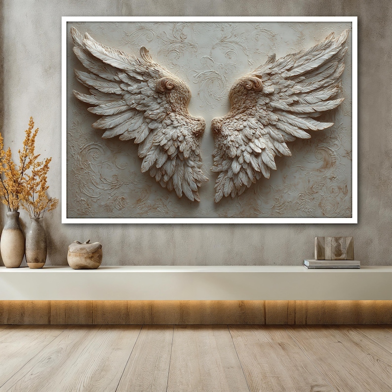 May include: A framed wall art piece featuring a pair of sculpted angel wings. The wings are a light beige color with detailed feather textures. The background has a subtle floral pattern. The artwork is displayed above a white shelf.