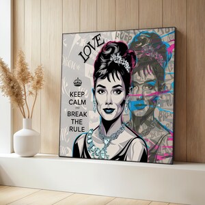Puede incluir: Impresión en lienzo de estilo pop art con un retrato de Audrey Hepburn con las palabras "LOVE", "KEEP CALM AND BREAK THE RULE". La obra de arte tiene un fondo gris con una segunda imagen más abstracta de Hepburn. El retrato es en blanco y negro con acentos azules y rosas.