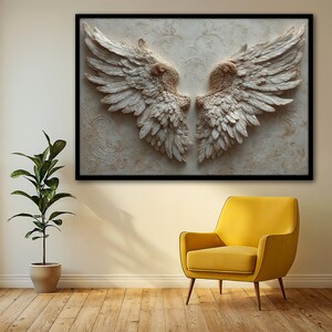 May include: A framed wall art piece featuring a pair of detailed, textured angel wings in shades of cream and beige. The wings are set against a textured background with a black frame. The artwork is displayed above a yellow armchair.
