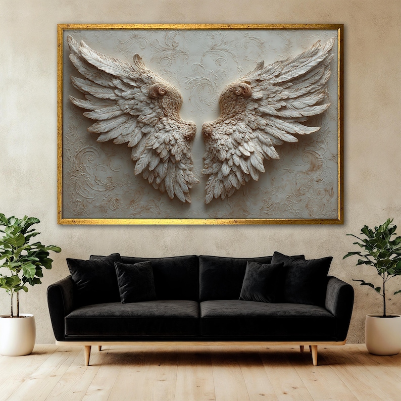 May include: A large framed artwork featuring a pair of sculpted angel wings in shades of white and beige. The wings are detailed with individual feathers and set against a textured background. The frame is gold, and the artwork hangs above a black sofa.