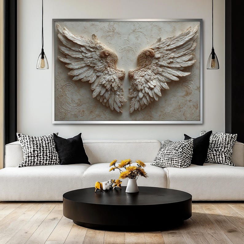 May include: A large, framed wall art piece featuring a pair of sculpted angel wings. The wings are a textured, off-white color, set against a neutral background with subtle patterns. The artwork is displayed above a white sofa with decorative pillows.