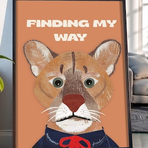 May include: Framed art print featuring a cougar illustration with the text "FINDING MY WAY" in white. The cougar has a brown and tan coat, green eyes, and a red nose. It wears a blue collar with a red bow.