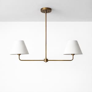 May include: A brass-coloured, two-light pendant light fitting with white, cone-shaped shades. The fitting has a central stem connecting to the ceiling and a horizontal bar with two curved arms holding the shades. The shades are white.