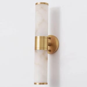 Puede incluir: Aplique de pared moderno con un diseño cilíndrico y aspecto marmóreo. Tiene detalles metálicos dorados, incluyendo bandas alrededor del centro y arriba/abajo. El aplique está montado sobre una placa circular dorada. Altura aproximada 40 cm.