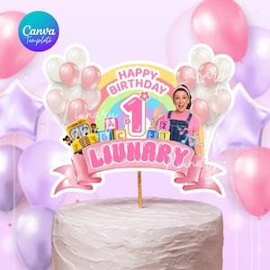 May include: A cake topper with a pink banner that reads "LIUNARY" and "HAPPY BIRTHDAY 1". The topper features a rainbow, balloons, and a cartoon image of a school bus and a woman. The cake is white with a textured surface.